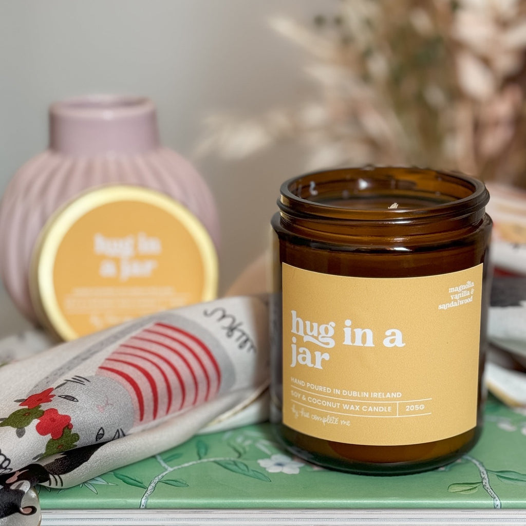 hug in a jar magnolia, vanilla and sandalwood scented best selling candle hand poured in Dublin, Ireland. In an amber jar with matching gold lid in an 8oz jar